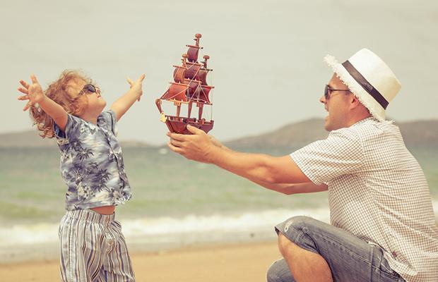 dad and little girl at beach, dad handing girl a wood, fully rigged sailing ship